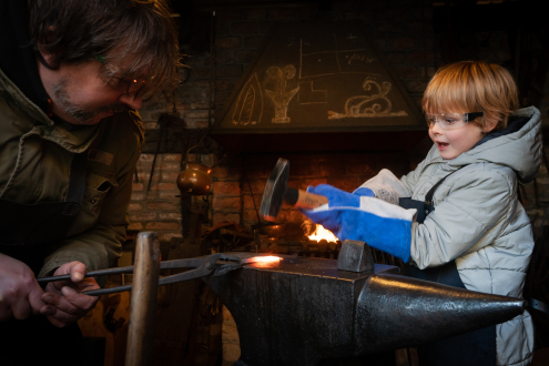 Man and child forge iron on the anvil
