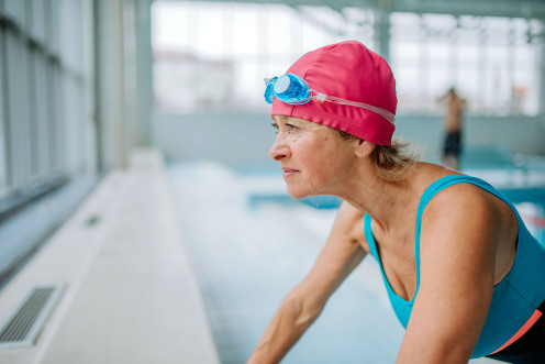 Actieve oudere vrouw die zich voorbereidt op het zwemmen in een overdekt zwembad.