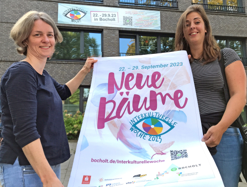 Caroine Blenker (links) und Julia Nakotte präsentieren das Plakat für die Interkulturelle Woche 2023