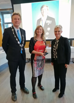  Anton Stapelkamp, burgemeester van de gemeente Aalten, eert Gerda Brethouwer (midden), directeur van het Nationaal Onderduikmuseum Aalten, met de Nederlandse Orde van Verdienste \