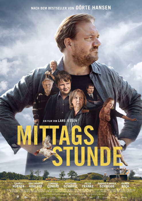 Der Hauptdarsteller steht in ländlicher Landschaft, blickt nachdenklich in die Ferne und hat die Hände in die Hüften gestemmt.